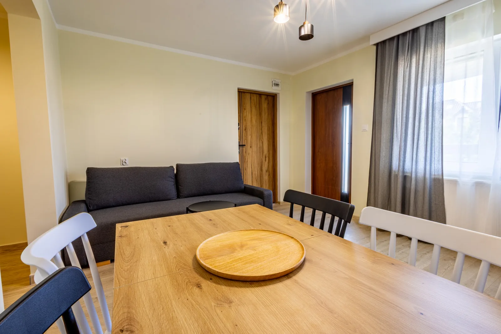 Drewniany stół w części jadalnej apartamentu z sofą w tle