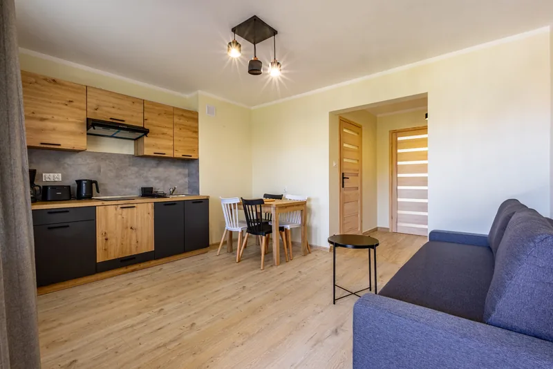 Jasny salon apartamentu z aneksem kuchennym i drewnianym stołem